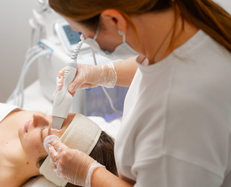 A beautician is cleaning a young woman's face with an ultrasonic spatula a facial scrubber a facial cleansing procedure in beauty salon