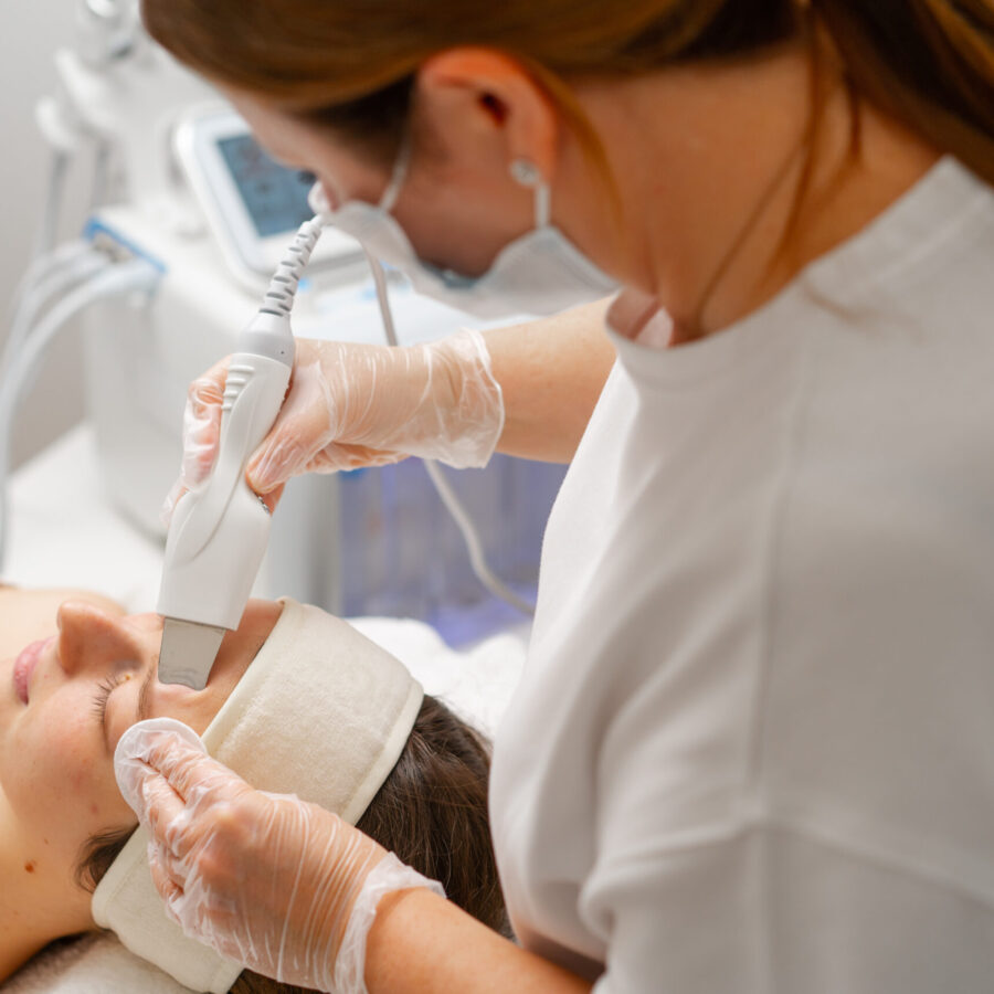 A beautician is cleaning a young woman's face with an ultrasonic spatula a facial scrubber a facial cleansing procedure in beauty salon