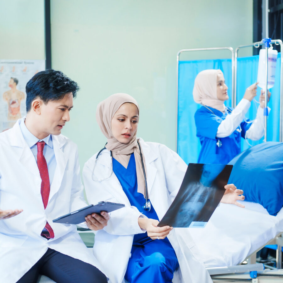 Two Muslim female doctors meet with an Asian male doctor to discuss an X-ray, blood vessel samples